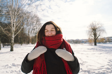 A woman with a red scarf enjoys a snowy winter day in a forest setting beneath a bright blue skyの写真素材