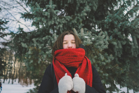 A woman with a red scarf enjoys a snowy winter day in a forest setting beneath a bright blue skyの写真素材