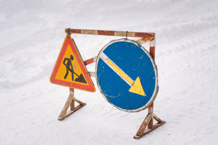 Construction and detour signs positioned in snowy environment indicating road work ahead in winterの写真素材