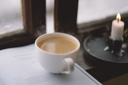 Cozy winter day with steaming coffee, open book, and candlelight by the snowy window