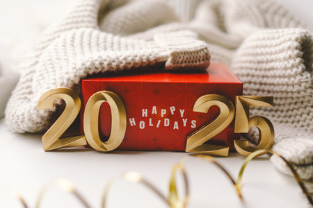 Red gift box with numbers revealing the New Year 2025, surrounded by cozy knitwear