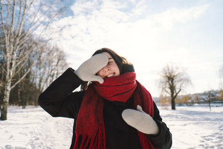 A woman with a red scarf enjoys a snowy winter day in a forest setting beneath a bright blue sky