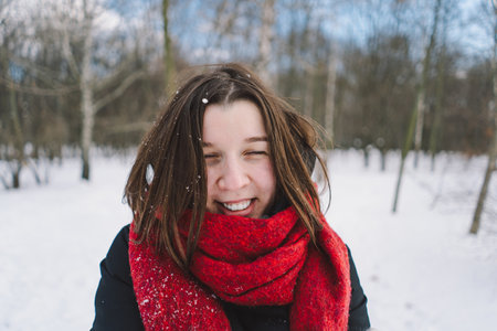 A woman with a red scarf enjoys a snowy winter day in a forest setting beneath a bright blue skyの写真素材
