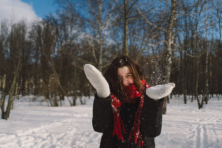 A woman with a red scarf enjoys a snowy winter day in a forest setting beneath a bright blue skyの写真素材