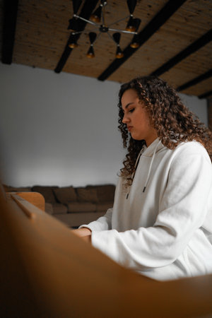 A woman with curly hair sits at a piano, enjoying the music she createsの写真素材