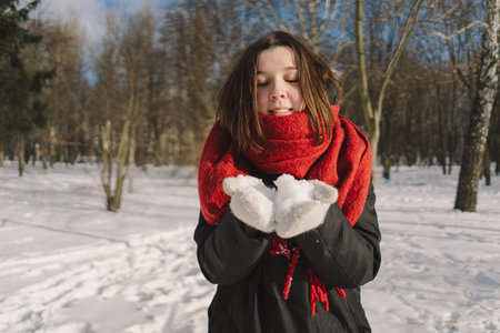 A woman with a red scarf enjoys a snowy winter day in a forest setting beneath a bright blue skyの写真素材
