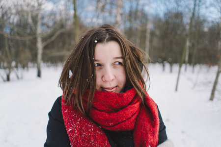 A woman with a red scarf enjoys a snowy winter day in a forest setting beneath a bright blue skyの写真素材