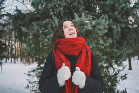 A woman with a red scarf enjoys a snowy winter day in a forest setting beneath a bright blue skyの写真素材