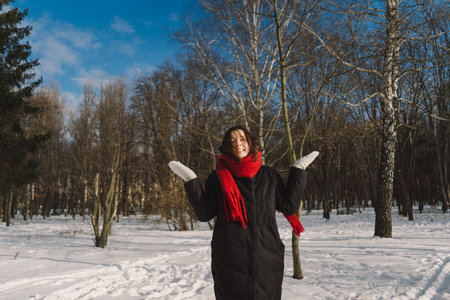 A woman with a red scarf enjoys a snowy winter day in a forest setting beneath a bright blue skyの写真素材