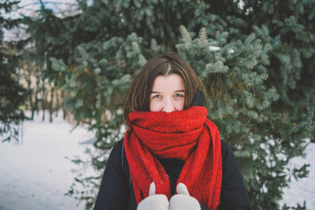 A woman with a red scarf enjoys a snowy winter day in a forest setting beneath a bright blue skyの写真素材