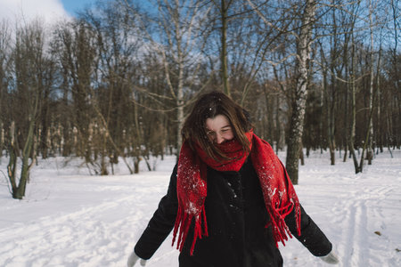 A woman with a red scarf enjoys a snowy winter day in a forest setting beneath a bright blue skyの写真素材