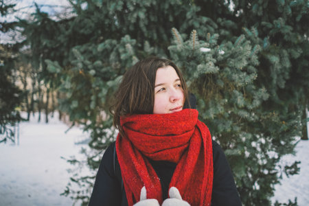 A woman with a red scarf enjoys a snowy winter day in a forest setting beneath a bright blue skyの写真素材