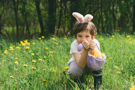 Boy with eggs basket and bunny ears on Easter egg hunt in sunny spring garden.の写真素材