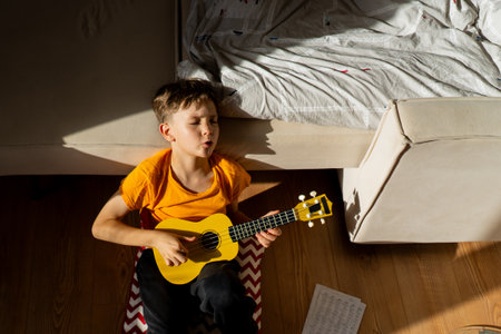 Boy playing a yellow ukulele while in his room at homeの写真素材