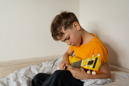 Boy playing a yellow ukulele while in his room at homeの写真素材