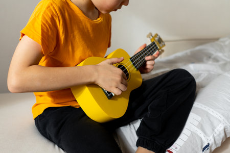 Boy playing a yellow ukulele while in his room at homeの写真素材