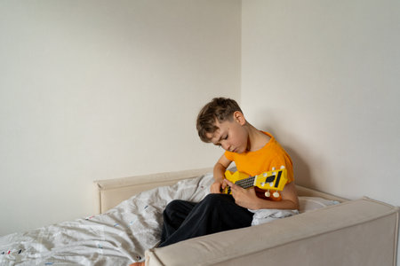 Boy playing a yellow ukulele while in his room at homeの写真素材