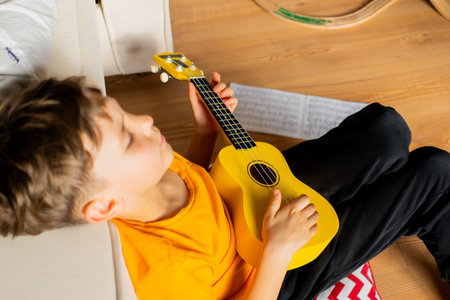 Boy playing a yellow ukulele while in his room at home