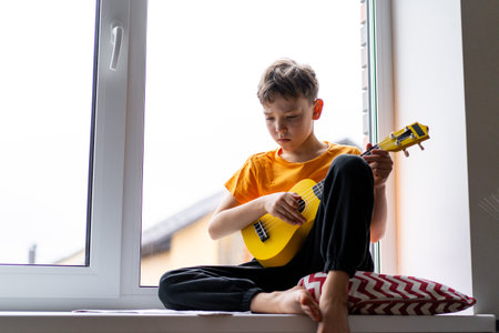 Boy playing a yellow ukulele while in his room at homeの写真素材