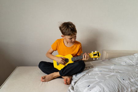 Boy playing a yellow ukulele while in his room at home