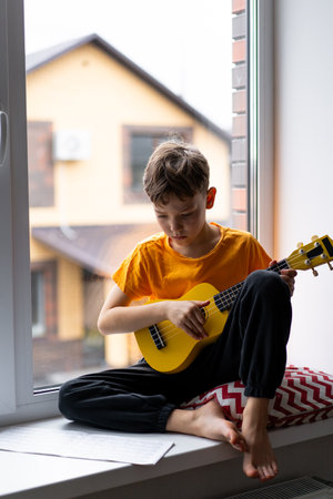 Boy playing a yellow ukulele while in his room at homeの写真素材
