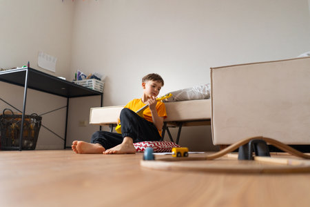 Boy playing a yellow ukulele while in his room at homeの写真素材