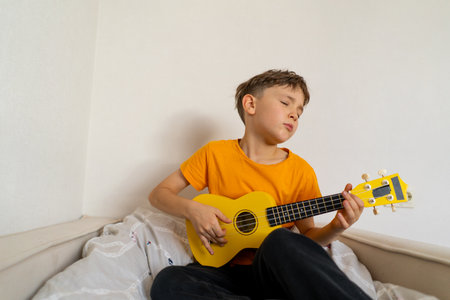 Boy playing a yellow ukulele while in his room at homeの写真素材