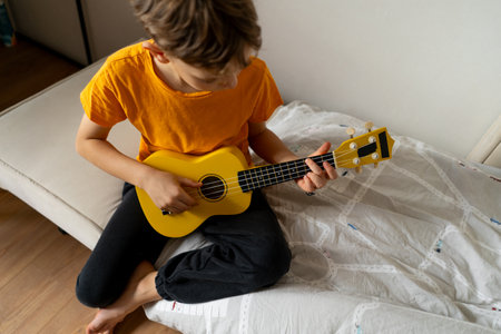 Boy playing a yellow ukulele while in his room at homeの写真素材
