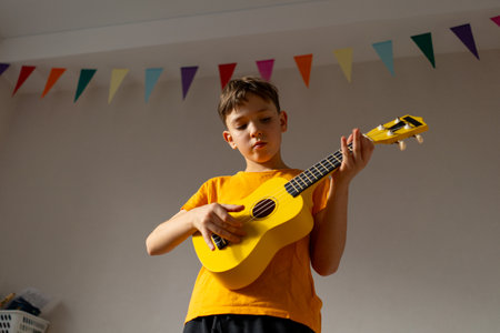 Boy playing a yellow ukulele while in his room at homeの写真素材