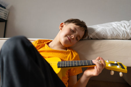 Boy playing a yellow ukulele while in his room at homeの写真素材