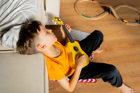 Boy playing a yellow ukulele while in his room at homeの写真素材