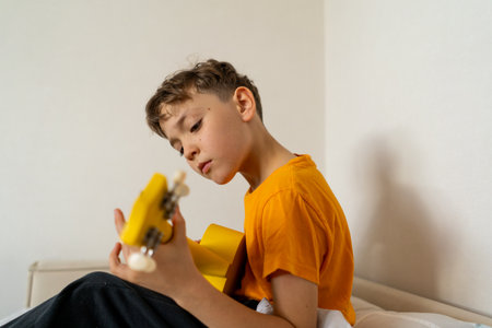 Boy playing a yellow ukulele while in his room at homeの写真素材