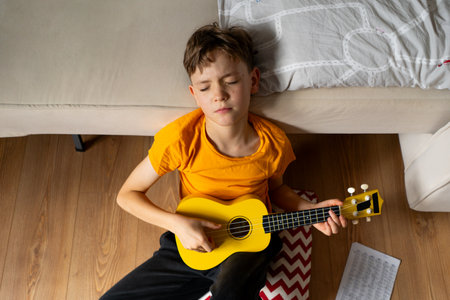 Boy playing a yellow ukulele while in his room at home