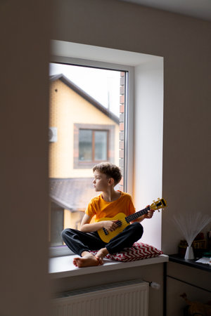 Boy playing a yellow ukulele while in his room at homeの写真素材