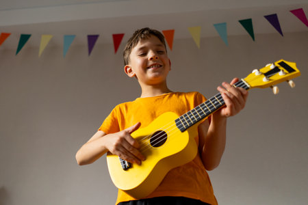 Boy playing a yellow ukulele while in his room at homeの写真素材