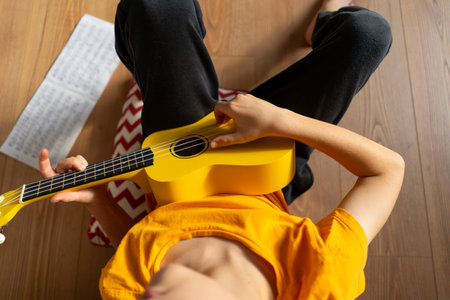 Boy playing a yellow ukulele while in his room at homeの写真素材