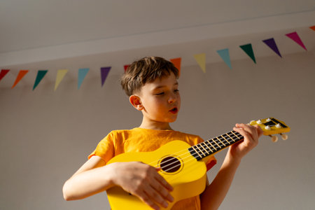 Boy playing a yellow ukulele while in his room at homeの写真素材