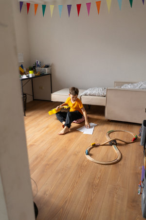 Boy playing a yellow ukulele while in his room at homeの写真素材