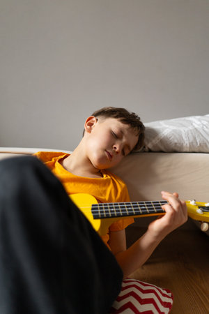 Boy playing a yellow ukulele while in his room at homeの写真素材