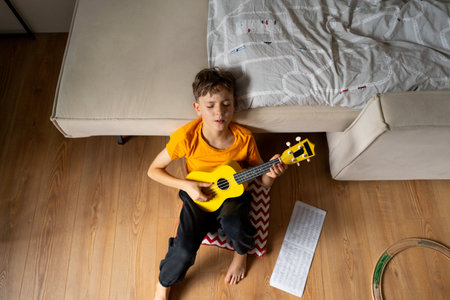 Boy playing a yellow ukulele while in his room at homeの写真素材