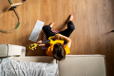 Boy playing a yellow ukulele while in his room at homeの写真素材