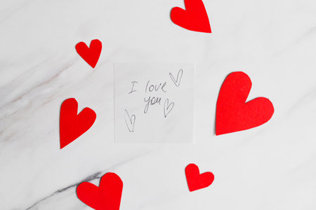 Romantic letter with a rose and heart confetti on a marble table ready for a special occasion.の写真素材