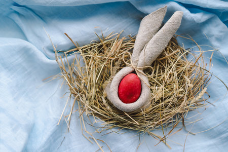 Colorful Easter eggs nestled in a nest surrounded by flowers and straw on a light blue backgroundの写真素材