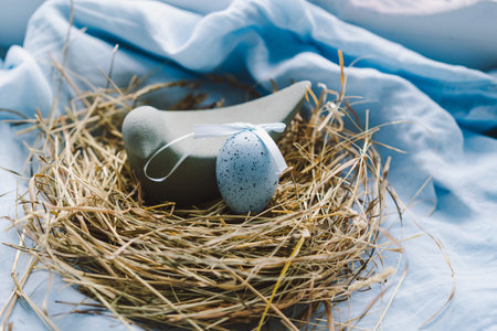 Colorful Easter eggs nestled in a nest surrounded by flowers and straw on a light blue backgroundの写真素材
