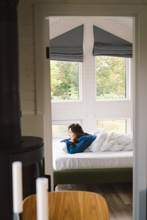 Joyful woman relaxing on soft white bed linen in a cozy bedroom during morning hoursの写真素材