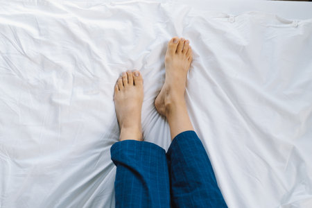 Relaxed feet resting on a clean, white bedspread in a calm bedroom environmentの写真素材