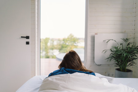 Joyful woman relaxing on soft white bed linen in a cozy bedroom during morning hoursの写真素材