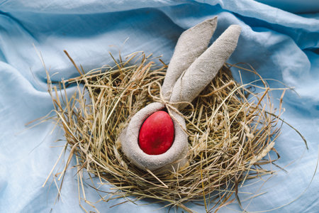 Colorful Easter eggs nestled in a nest surrounded by flowers and straw on a light blue backgroundの写真素材