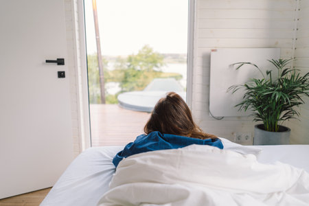 Joyful woman relaxing on soft white bed linen in a cozy bedroom during morning hoursの写真素材