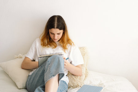 A teenage girl is drawing or doing homework in the bedroom. A teenager studies at home.の写真素材